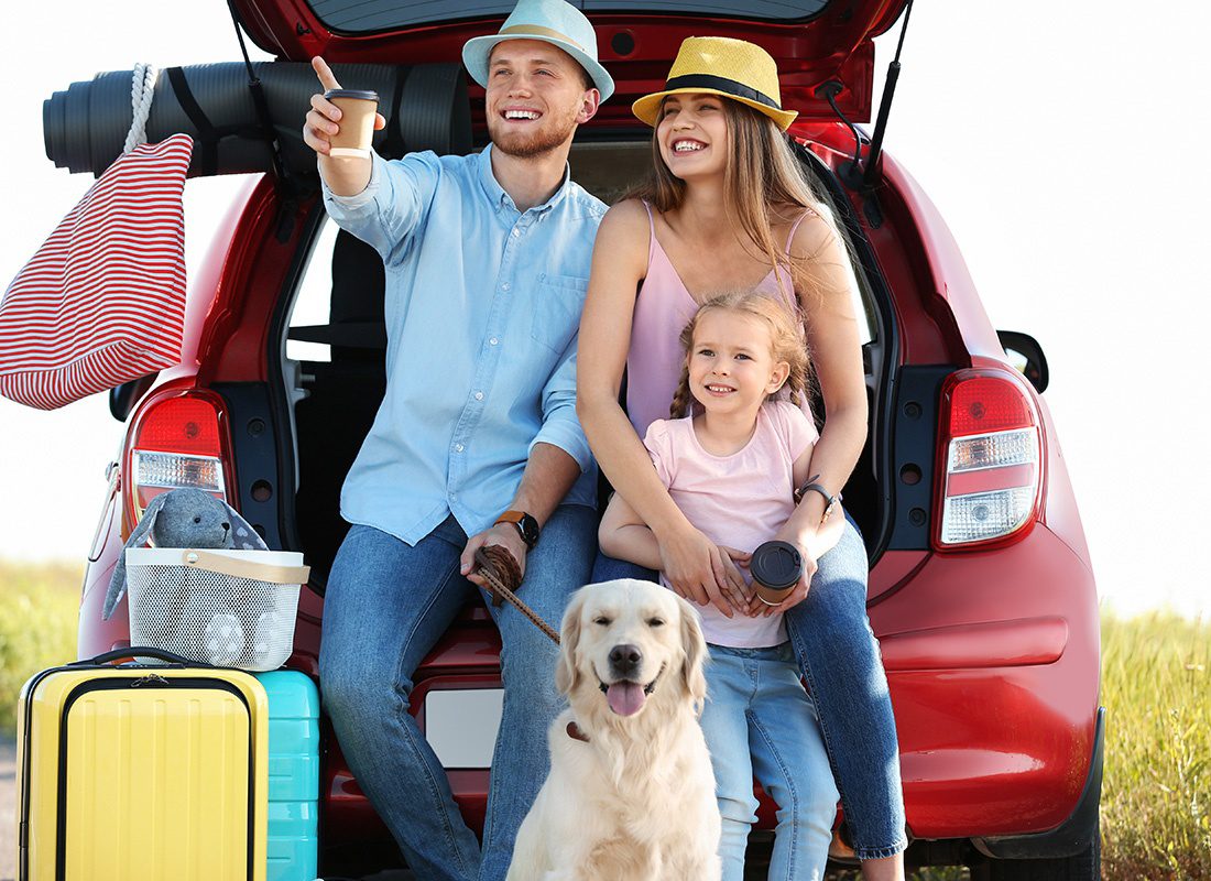 Personal Insurance - Happy Family With Their Dog Sitting at the Back of Their Red Car on a Road Trip